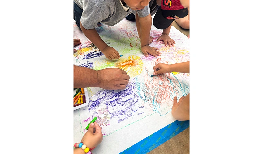 view from above of several pairs of hands working with crayons on a big piece of paper